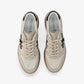 A low-top platform sneaker by Premiata, featuring a cream and beige suede and mesh upper, a black cross logo on the side, gold-tone hardware, and a thick tan gum sole.